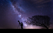 Man with telescope silhouetted against a starry sky