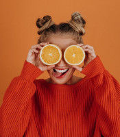 Women in orange jumper holding cut oranges over her eyes