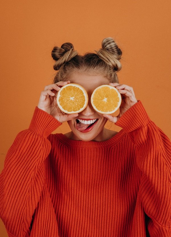 Women in orange jumper holding cut oranges over her eyes