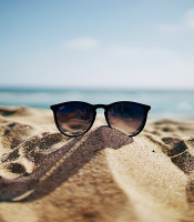 Sunglasses on a sand dune through which you can see the ocean and blue sky