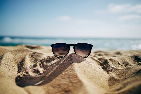 Sunglasses on a sand dune through which you can see the ocean and blue sky